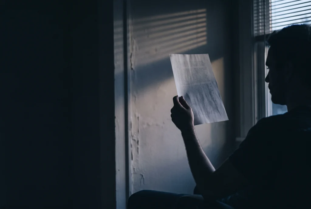A single sheet of paper held up to a window at dusk, the print unreadable against the light.